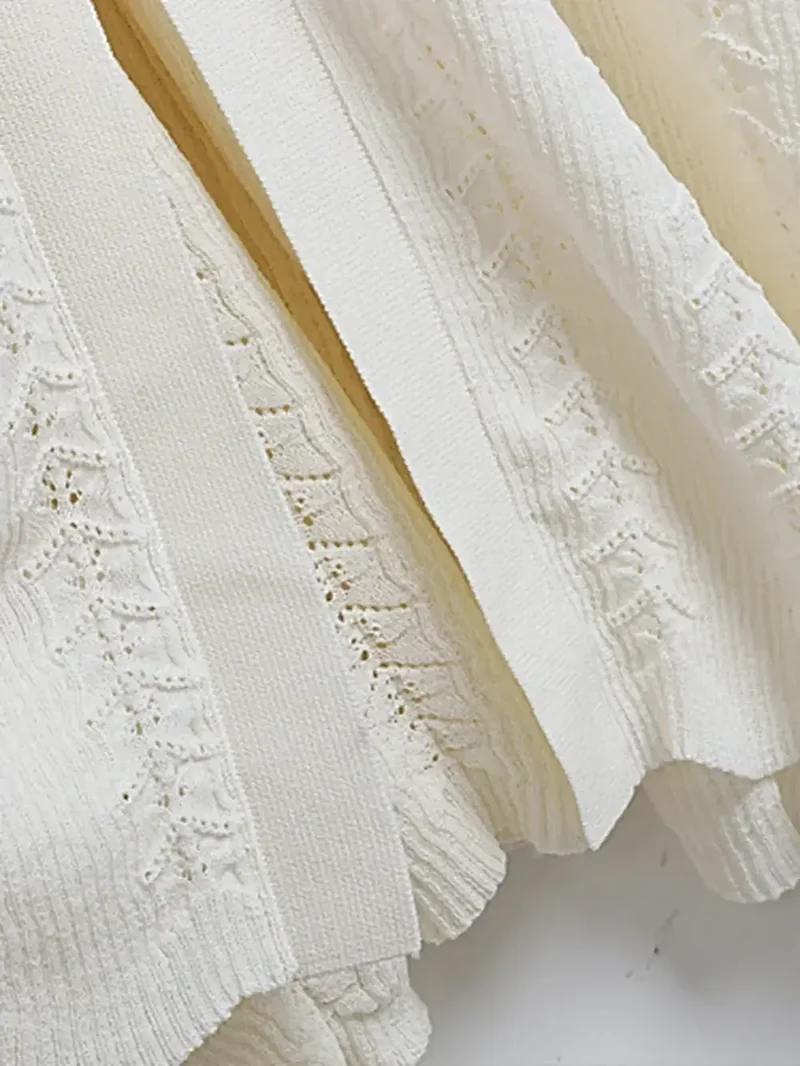 Elegante gebreide jurk met opengewerkte details, decoratieve knopen, ronde hals en lange mouwen.