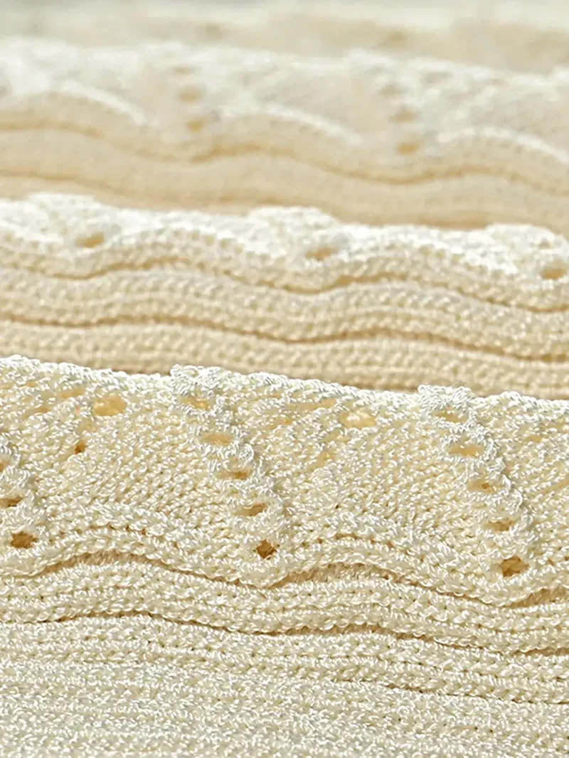 Elegante gebreide jurk met opengewerkte details, decoratieve knopen, ronde hals en lange mouwen.